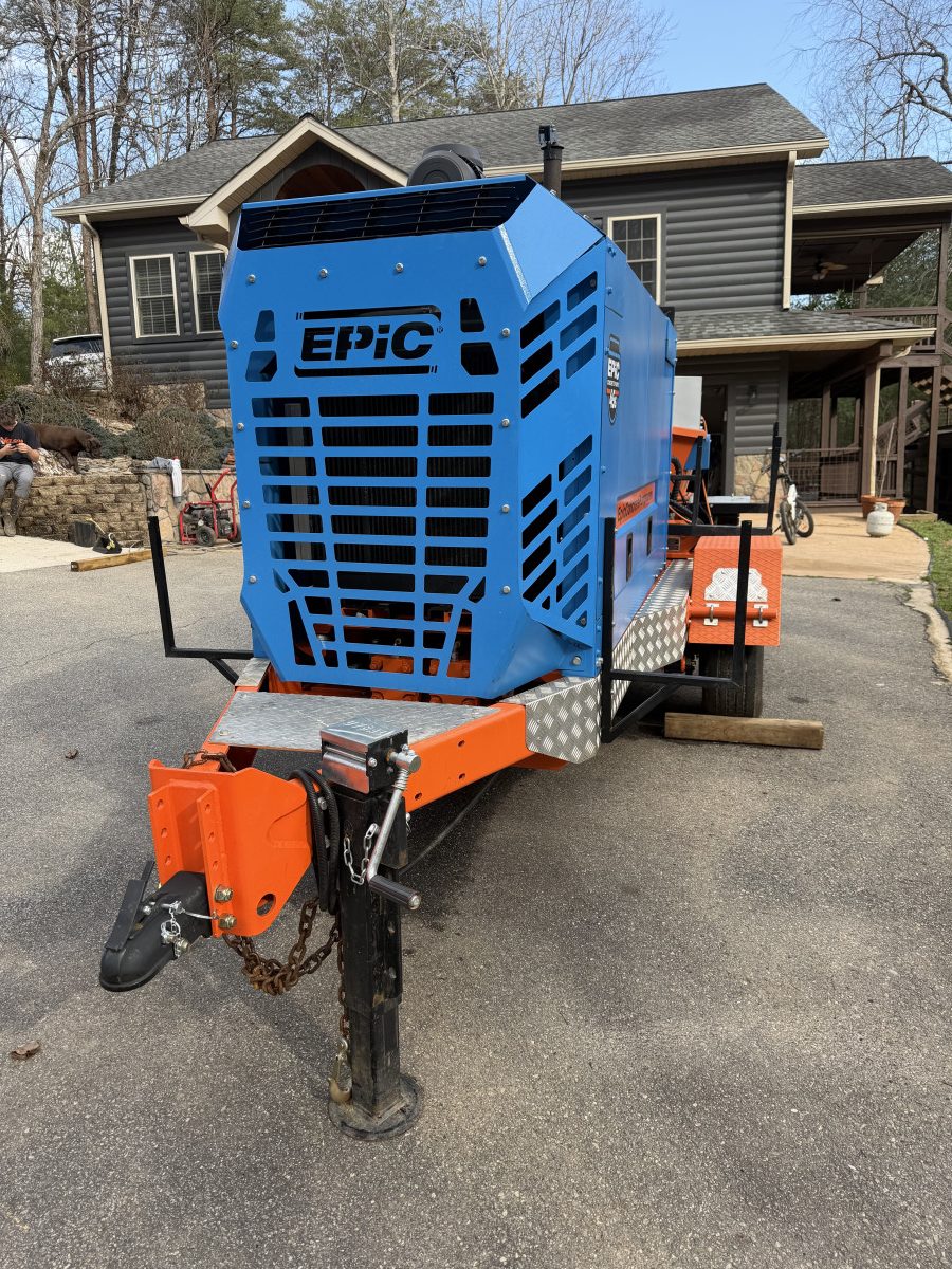 IMG_0221 – Thomas Concrete Machinery Blue EPIC wood chipper mounted on an orange trailer in a residential driveway beside a house, ready for use.